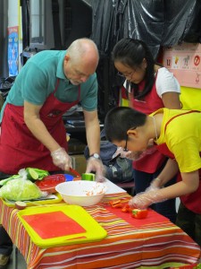 Teacher showing two students how to cut vegetables for cooking.
